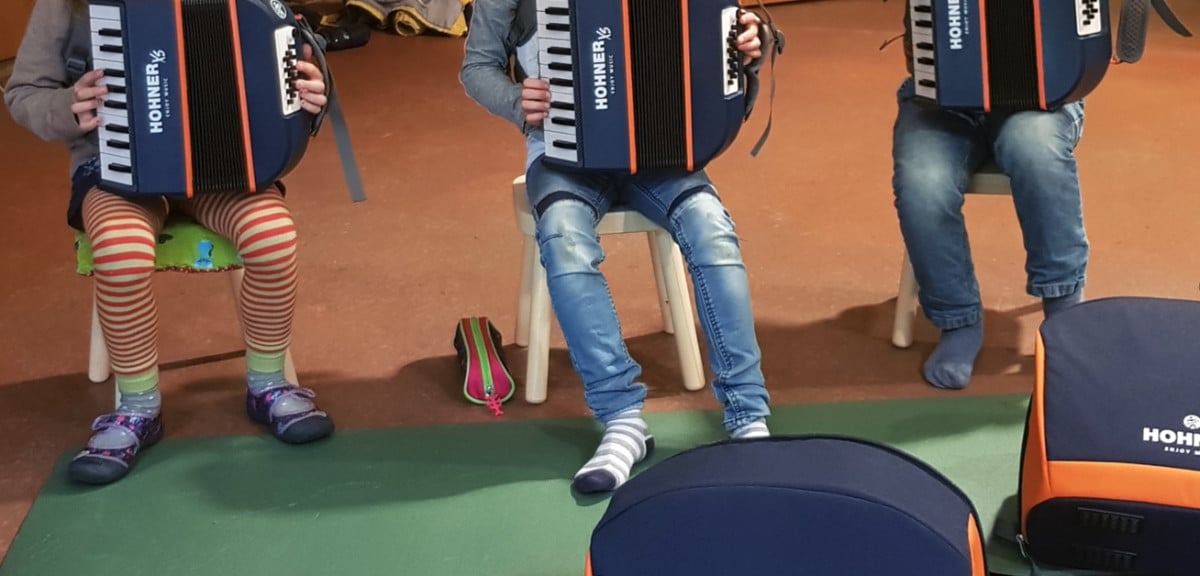 3 Kinder sitzen mit kleinen Akkordeons auf Stühlen